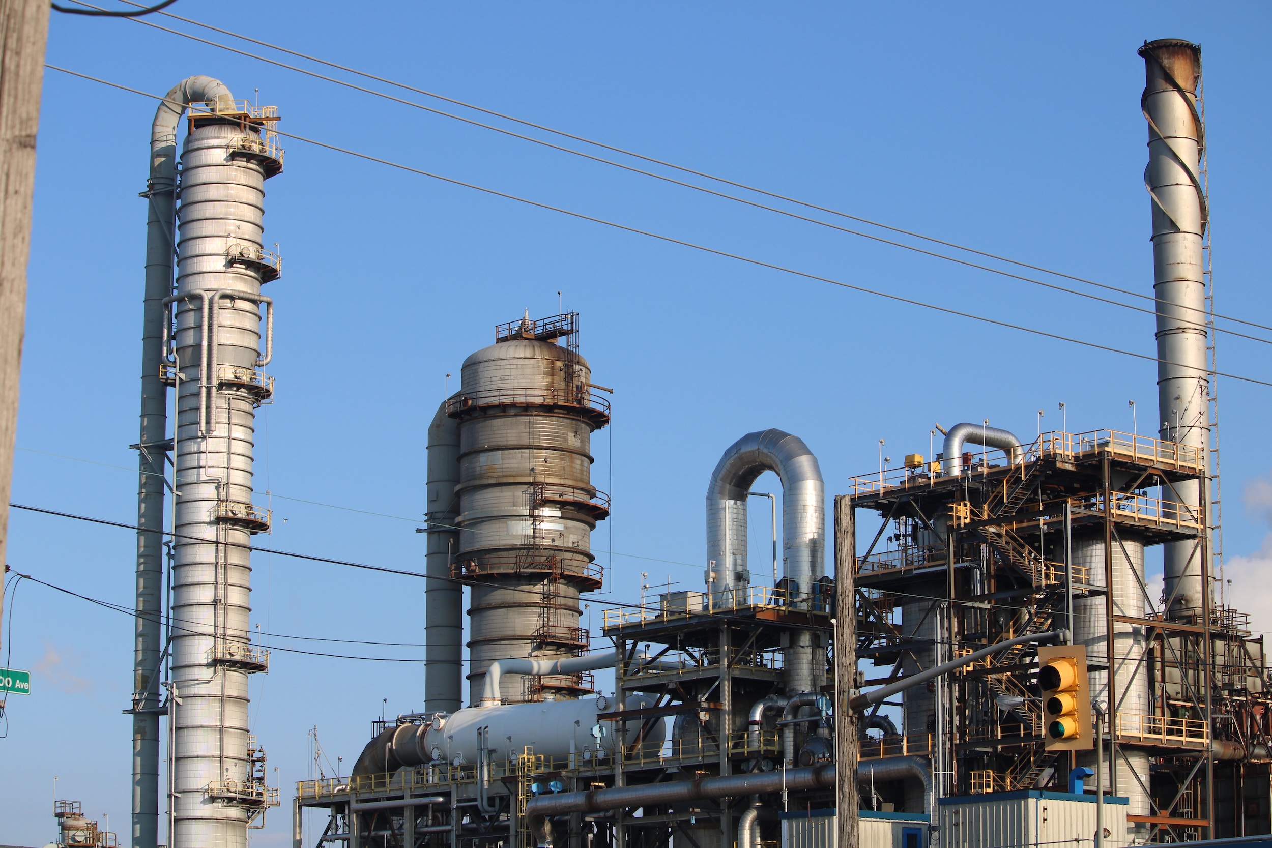 An industrial plant with large metal pipes, tubing and scaffolding is framed in blue sky.