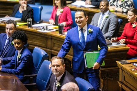 Manitoba budget: Premier Wab Kinew, in a blue suit, walks into the chamber of already seated representatives on budget day