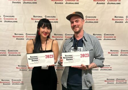 Cara McKenna and Mitt Simmons pose for a photo, holding award plaques, in front of a National Newspaper Awards backdrop