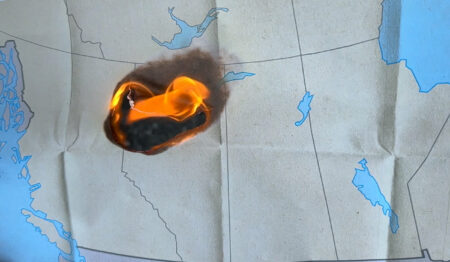 A paper map of western Canada that is on fire.