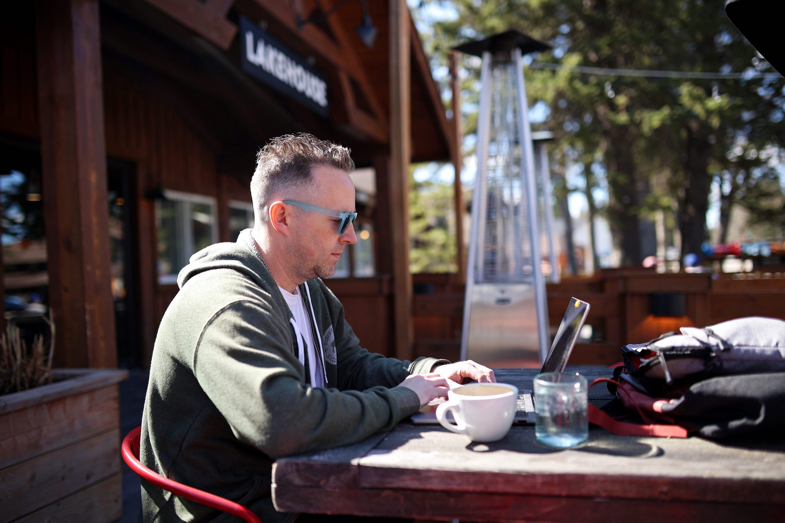 Riding Mountain National Park: a man in sunglasses sits outside in the sun while working on a laptop with a coffee cup next to him