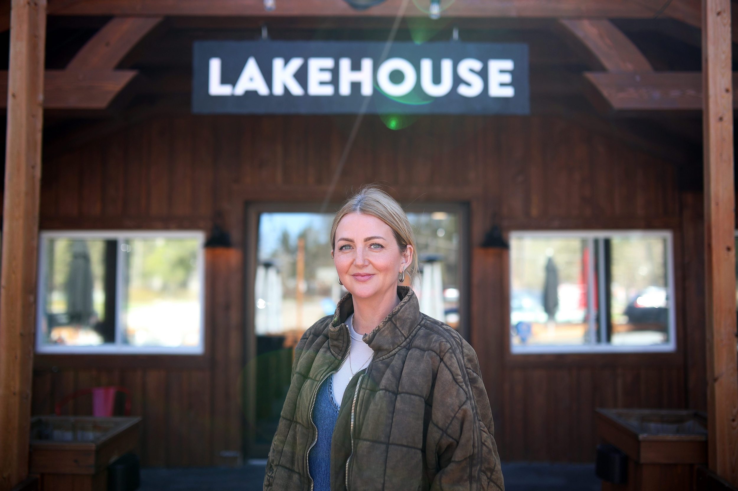 Riding Mountain National Park: A woman in a jacket stands looking at the camera in front of a log building with a sign reading "Lakehouse"