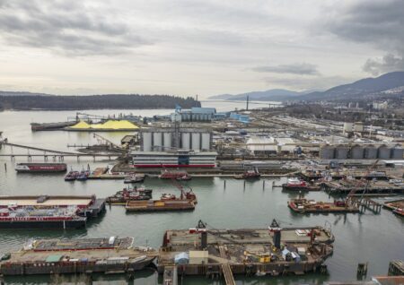 Burrard Inlet map: A wide view over an industrial area in the Burrard Inlet, including the Seaspan Ship Yard. There are a number of barges, piers and industrial facilities, with ocean and low mountains on the horizon.