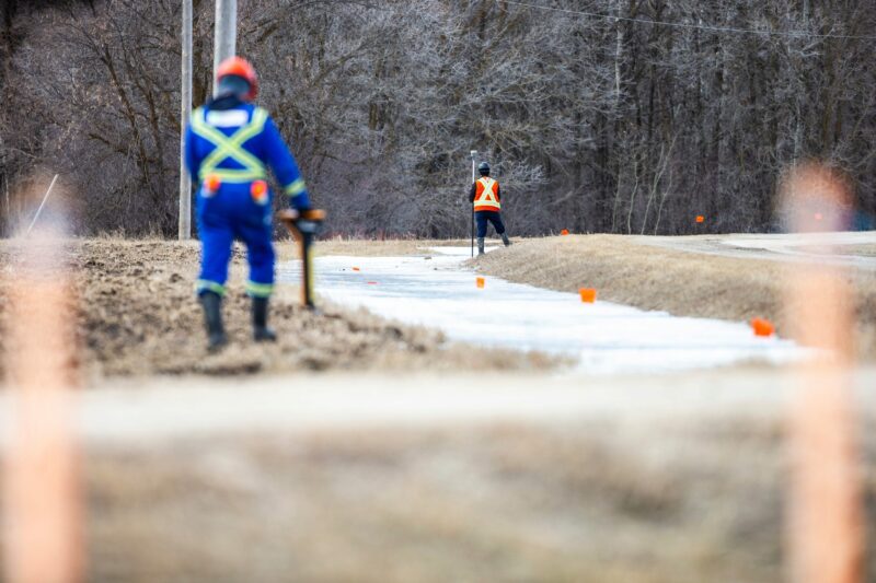 Two crew members in high visibility safety clothing stand along the path of Imperial Oil's Winnipeg Products Pipeline in southern Manitoba during repairs in March 2024