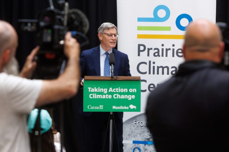 MP Terry Duguid (Winnipeg South) speaks at a news conference while journalists look on. A sign on the lectern reads "taking action on climate change"