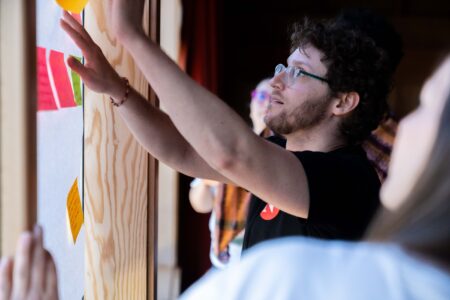 Arik Ligeti arranges sticky notes on a wall while others look on