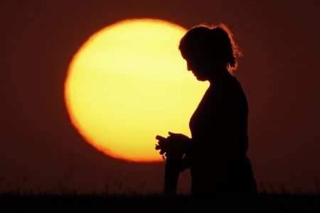 A woman silhouetted against the setting sun at the close of a hot summer day.