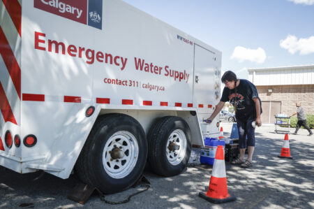 A person fills a water jug from a City of Calgary truck labelled "Emergency Water Supply"