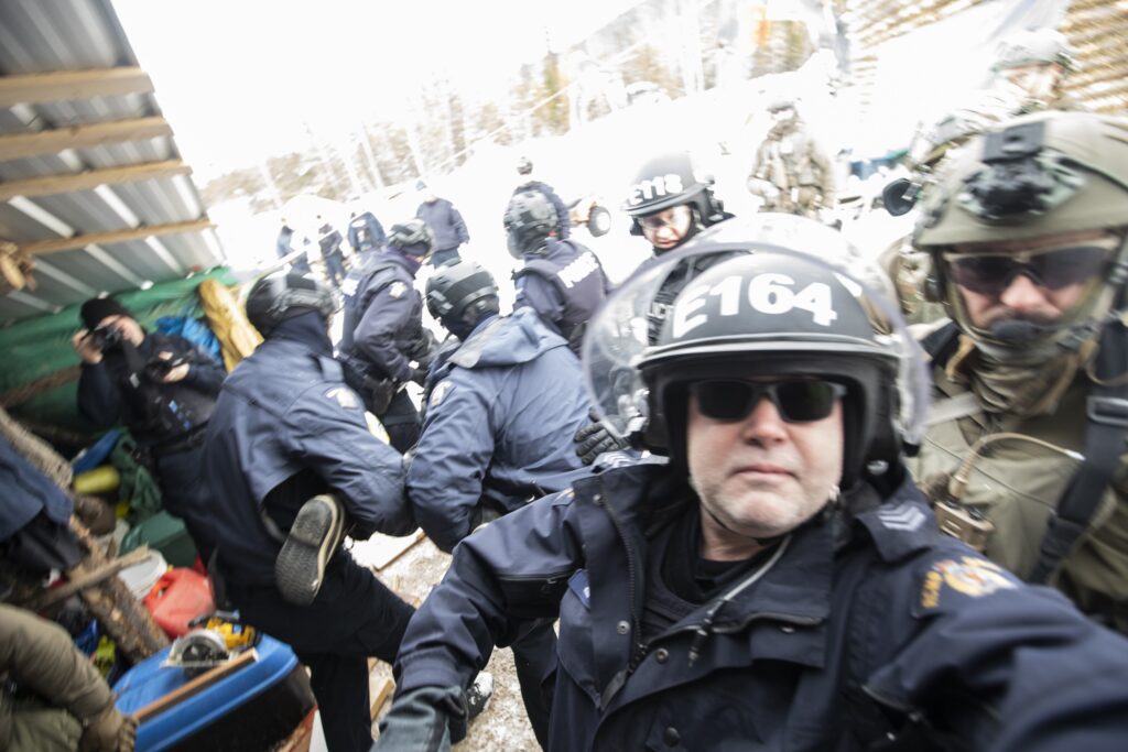 A crowd of police, including militarized police wait in the courtyard outside of a tiny house dwelling as supporters are arrested at Coyote Camp in Gidimt’en territory near Houston, BC on Friday, November 19, 2021.