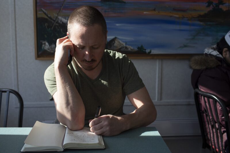 Narwhal reporter Drew Anderson sits at a table, writing in a notebook.