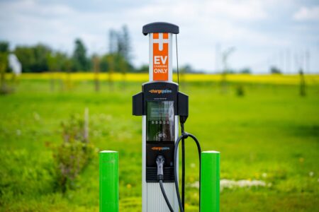 An electric vehicle charging station flanked by green posts in a grassy area in rural Manitoba