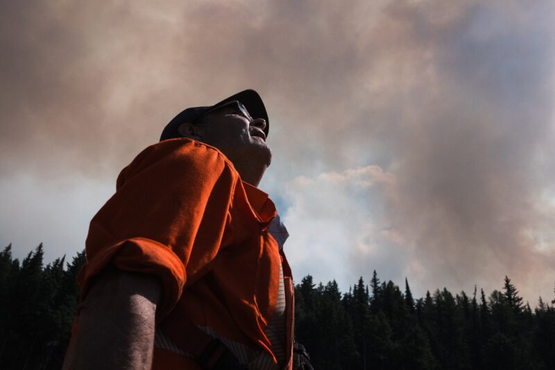 A man in an orange shirt looks up at smoke-filled skies