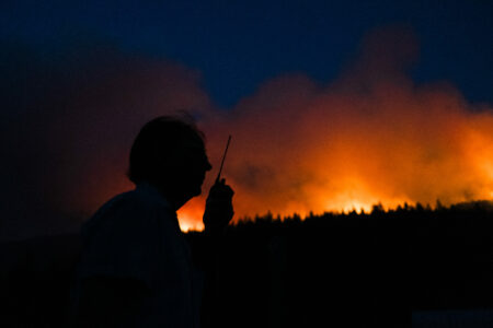 the silhouette of a volunteer firefighter in Argenta is framed by glowing red flames from the B.C. wildfire in the Kootenays.