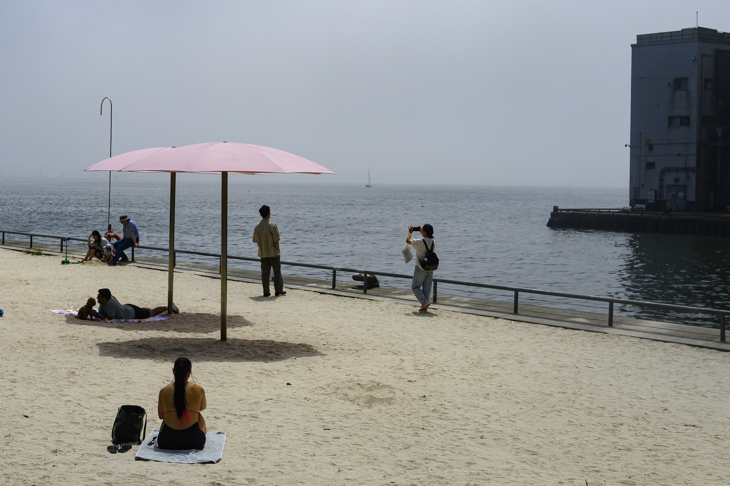Heat wave: people lounge in beach under pink umbrellas in the sand overlooking haze on Lake Ontario.