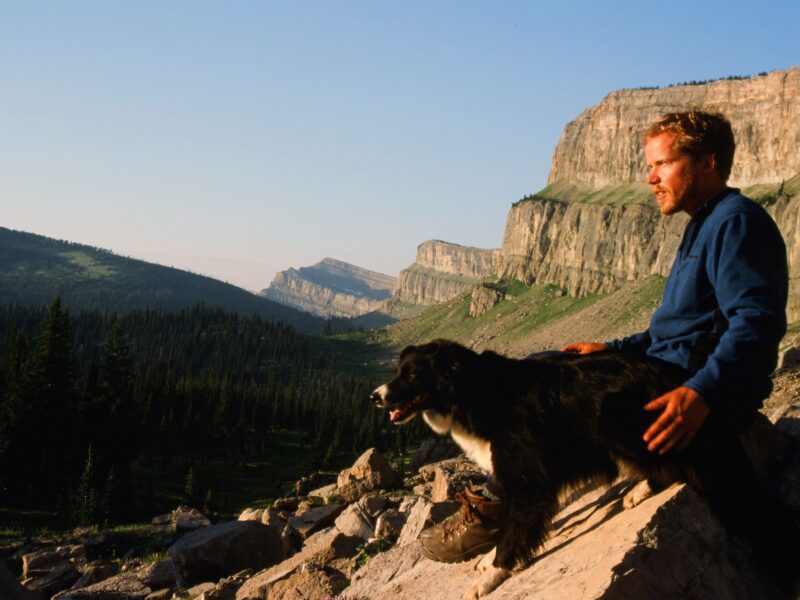 A vintage-looking photo of a hiker and a dog looking out over a valley in Montana’s Bob Marshall Wilderness