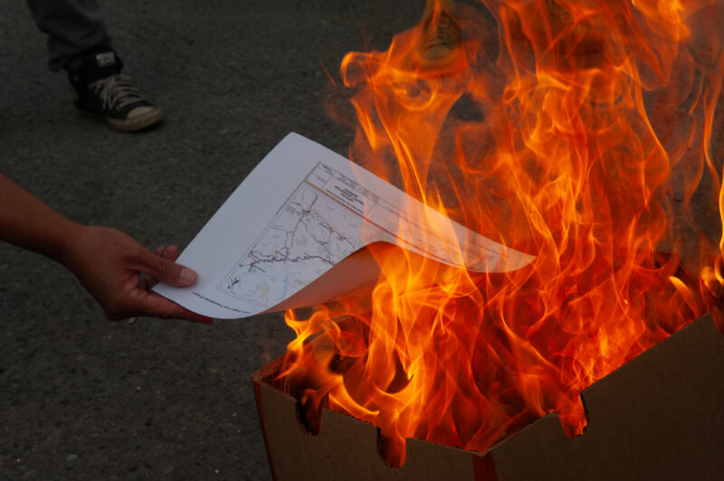 A Gitanyow community member feeds a page from a pipeline benefits agreement to a fire on Aug. 22, 2024