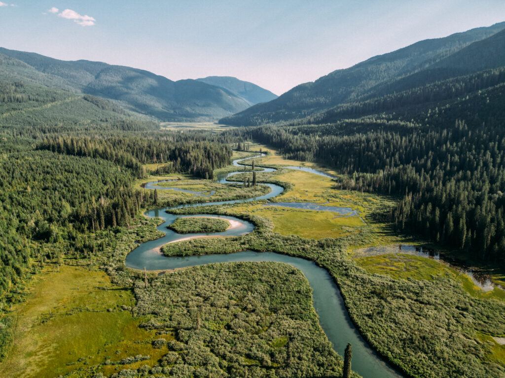 A blue-green river meaders through a valley flanked by treed mountain slopes