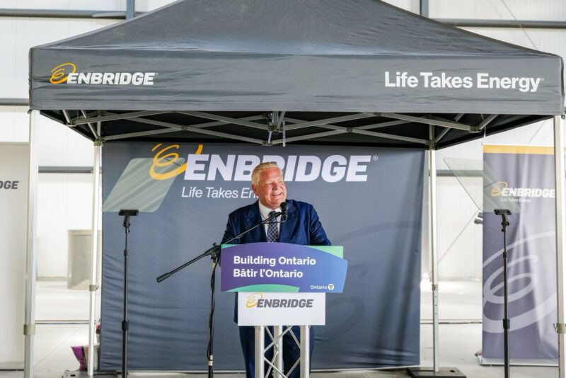 Ontario Premier Doug Ford stands at a podium that reads Building Ontario, with an Enbridge sign below it and under a tent that's labelled Enbridge