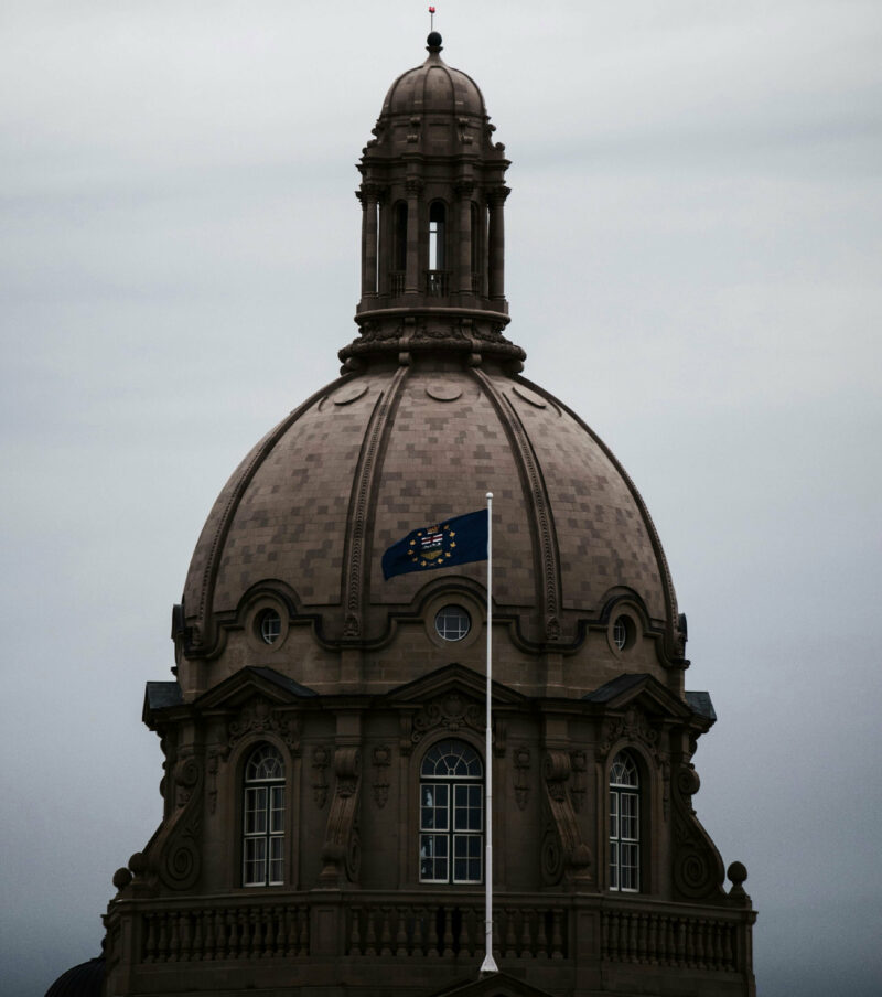 Moody photo of the peak of the Alberta legislature with Alberta flag visible