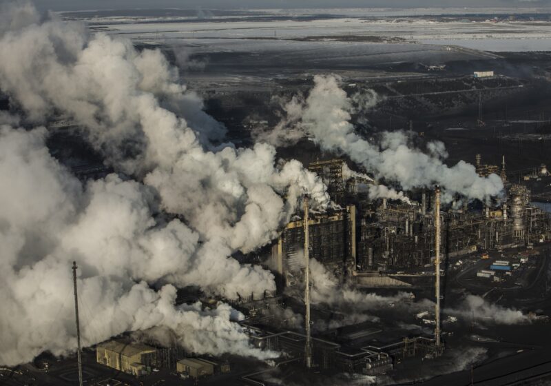 smoke or vapour billows from several tall smokestacks in a sprawling industrial area.