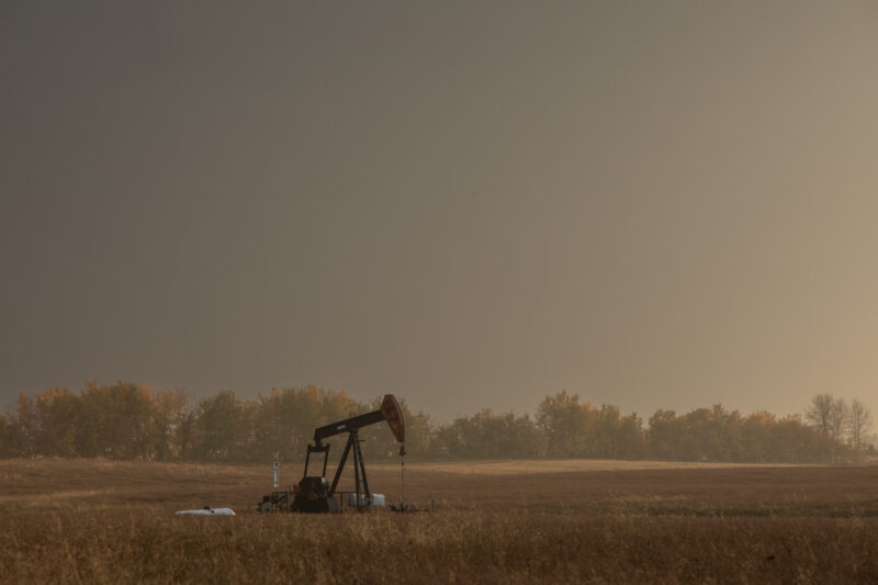 Pumpjack in a field bathed in golden twilight set against a distant treeline.