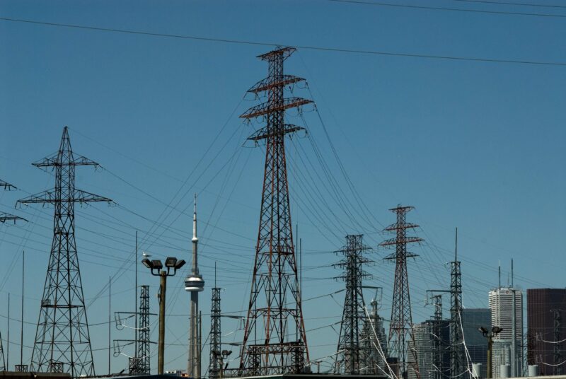 The CN Tower and a few other towers in the Toronto skyline peak between a transmission line on a clear blue sky