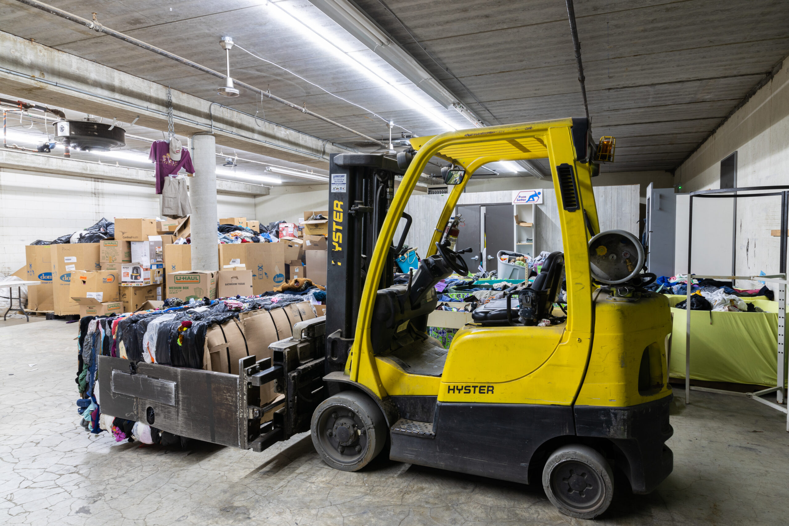 A yellow forklift holds a bale of compressed clothing and cardboard boxes in a Winnipeg thrift warehouse
