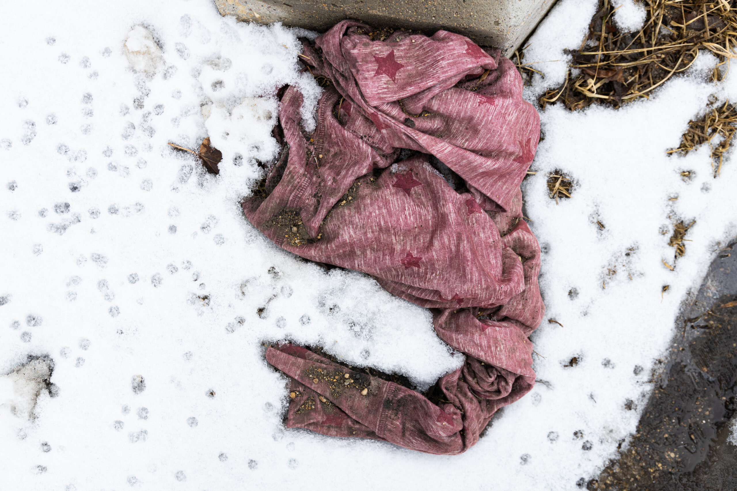 A piece of clothing with pink stripes and stars sits discarded in snow and dirt 
