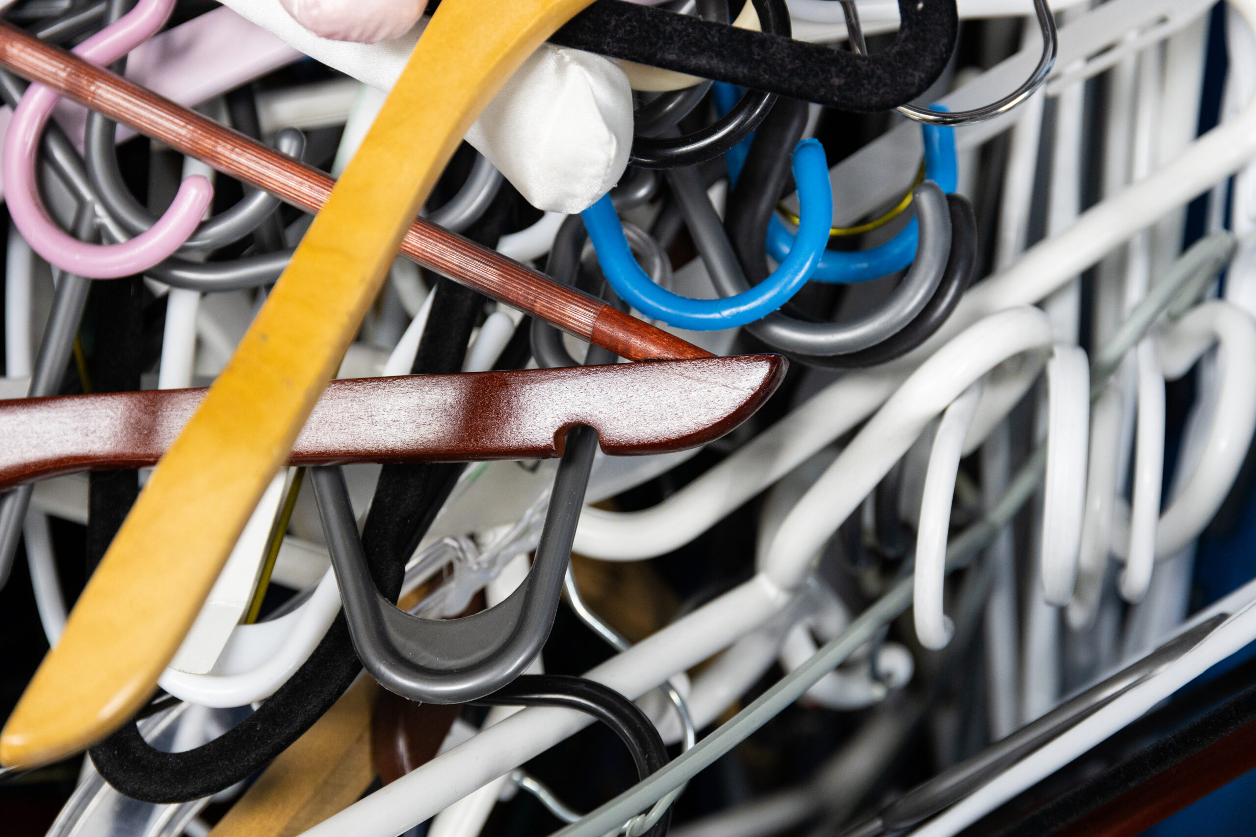A close up of a pile of white, black, pink, blue and brown clothing hangers
