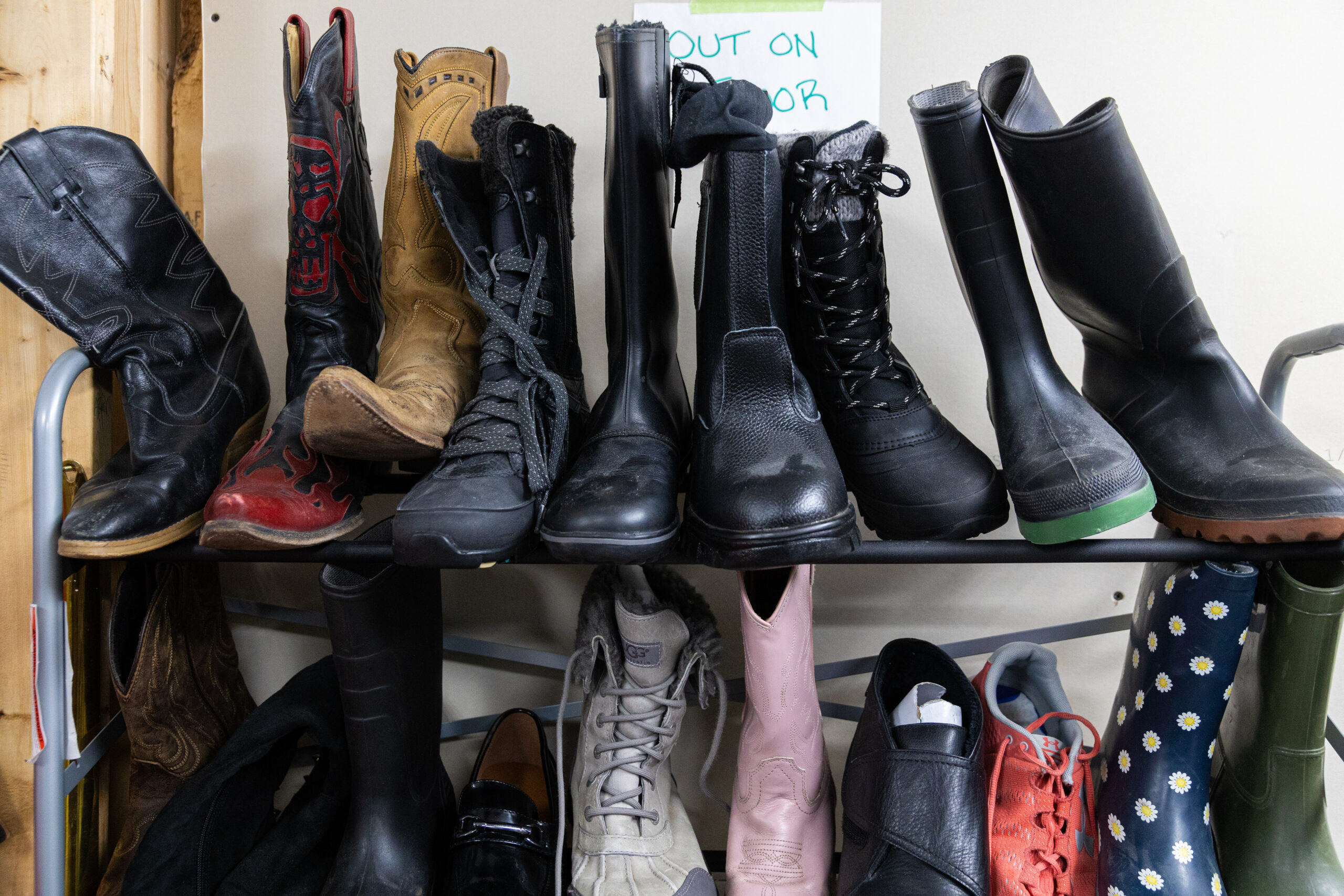 Several individual boots, including black, brown and pink leather cowboy boots, rubber boots and lace-up winter boots in the back room of a Winnipeg thrift store
