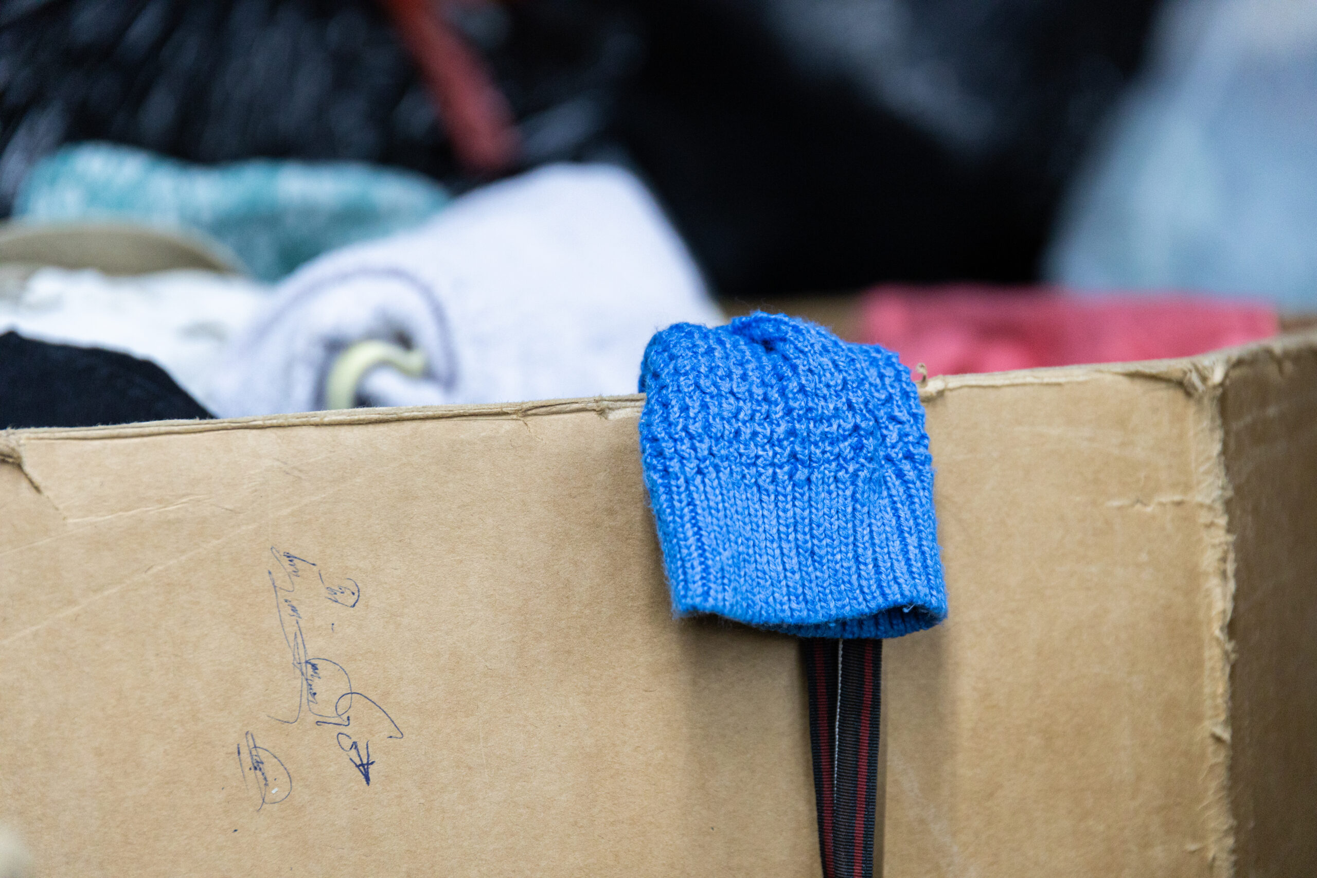 A bright blue knit sweater sleeve hangs over the edge of a cardboard box in a Winnipeg thrift warehouse
