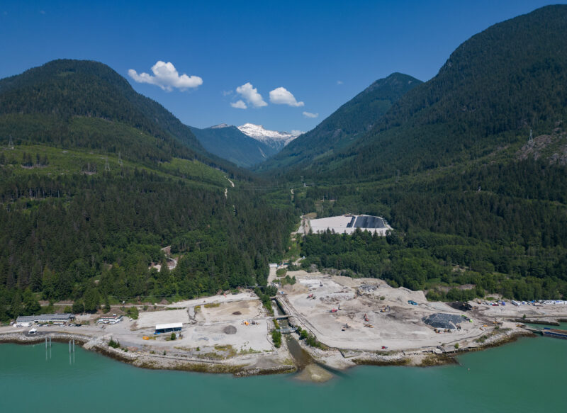 aerial view of the woodfibre LNG site with the greeny blue waters of howe sound in the foreground and the mountains behind