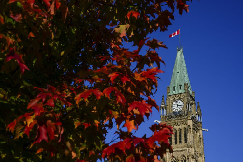 a close up of the peace tower on parliament hill framed against a trees, with leaves turning red
