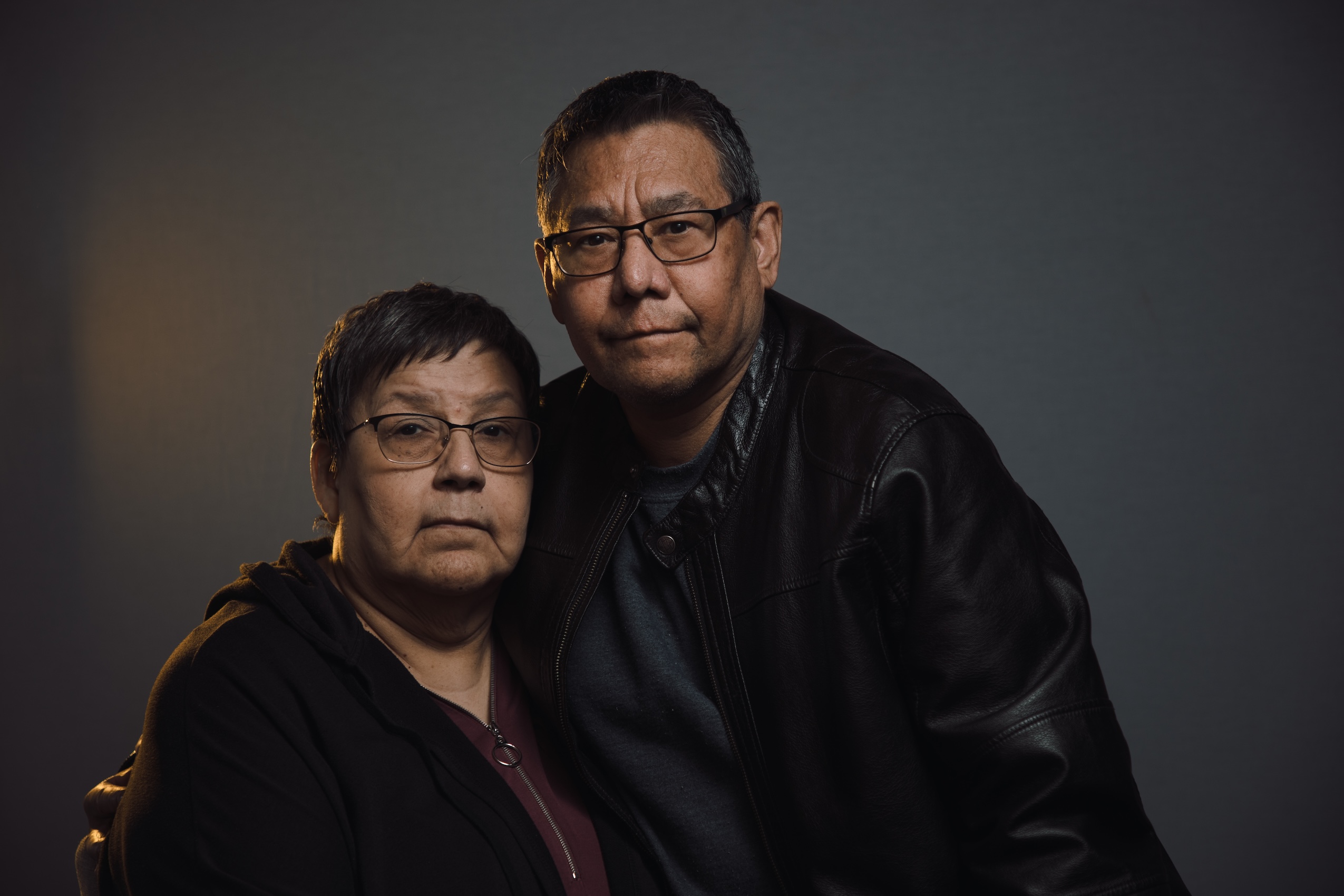Claire Cardinal and Kenneth Whiteknife pose for a sombre photo. She is seated and his arm is around her.