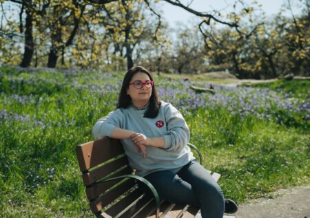 Kyla Fitzgerald, wearing a grey sweater with a Narwhal logo, sits on a park bench