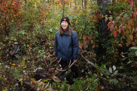 Steph Kwetásel’wet Wood smiles in a forest next to a moose that has been recently shot