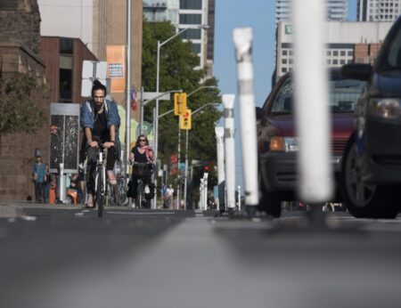 Cyclists in a busy Toronto bike lane along Bloor Street West, seen from ground level with cars just out of focus