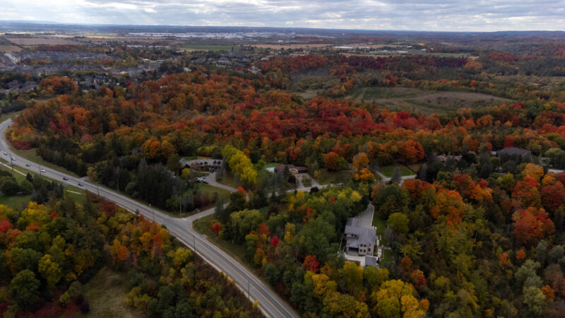 Highway 413: An aerial view of a road winding through fall foliage with a suburb in the distance