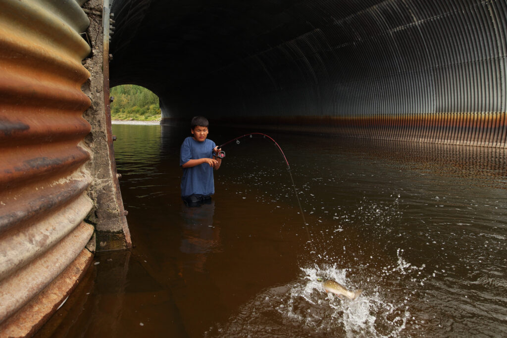 a ten year old uses a fishing rod in a large culvert in a river, with a big splash indicating a fish