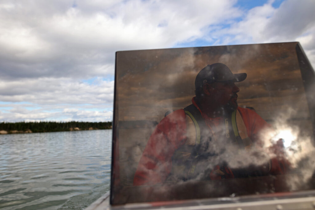 A man is seen through a coloured boat window as he drives it on a river