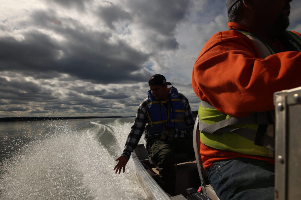 A man reaches out to touch the spray of a boat with grey clouds in the sky