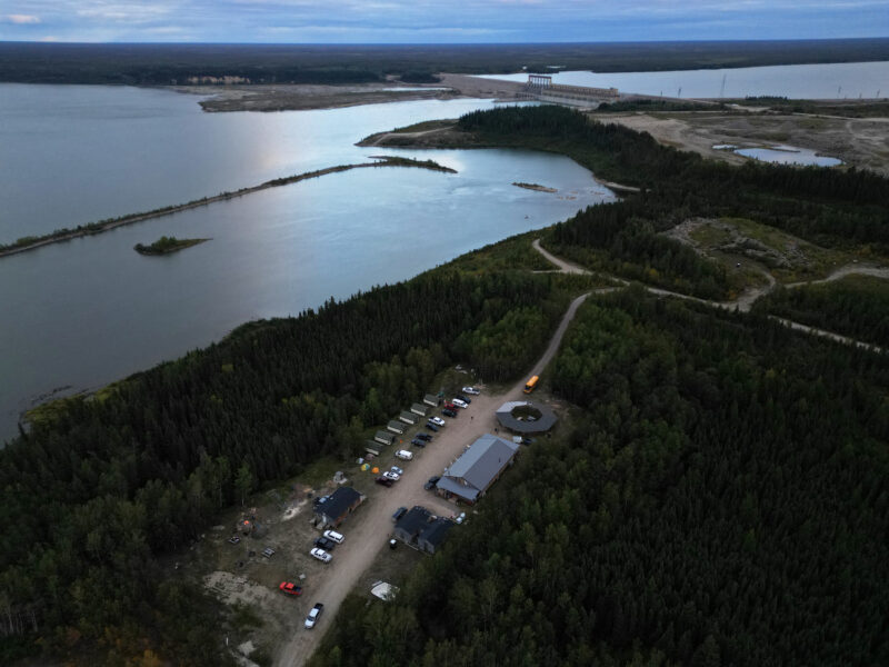 The Kitaskeenan Kaweekanawaynichikatek Fox Lake Cree Nation Culture Camp is seen from above near a large body of water with a dam visible in the near distance