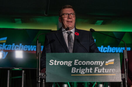 Scott moe behind a podium reading "strong economy bright future" speaking about Saskatchewan election results