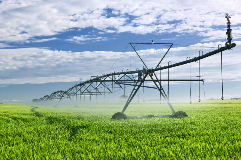 An irrigation arm sprays water on a farmed field.