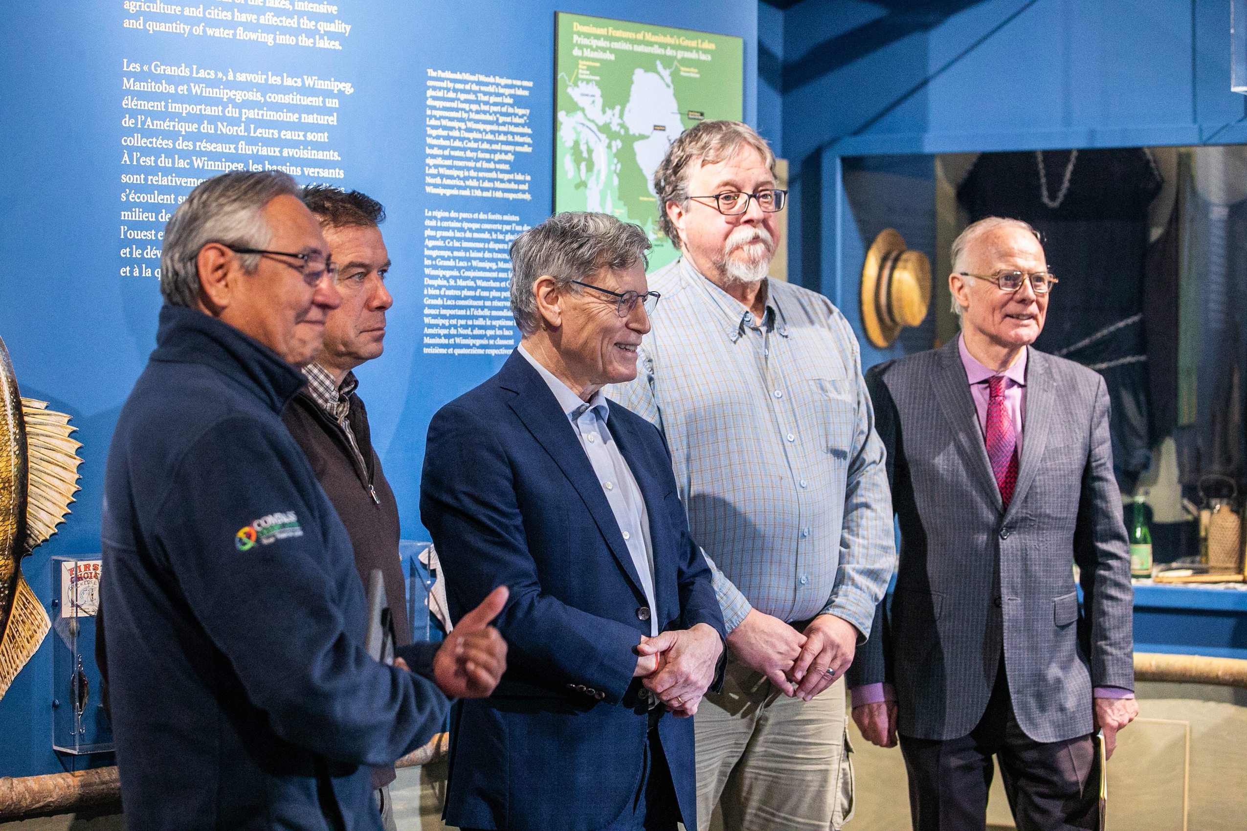 Elvin Huntinghawk (left), Ryan Canart, Terry Duguid, Don Huisman, and Jon Gerrard pose for a photo in a lake-themed exhibit at the Manitoba Museum after a funding announcement for an ecological corridor in the province