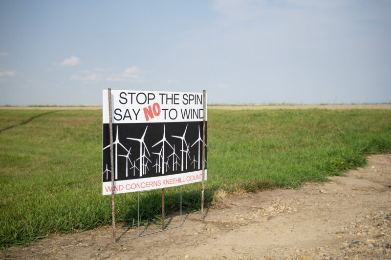 A sign that reads 'stop the spin, say no to wind' on the side of a rural road in Alberta.