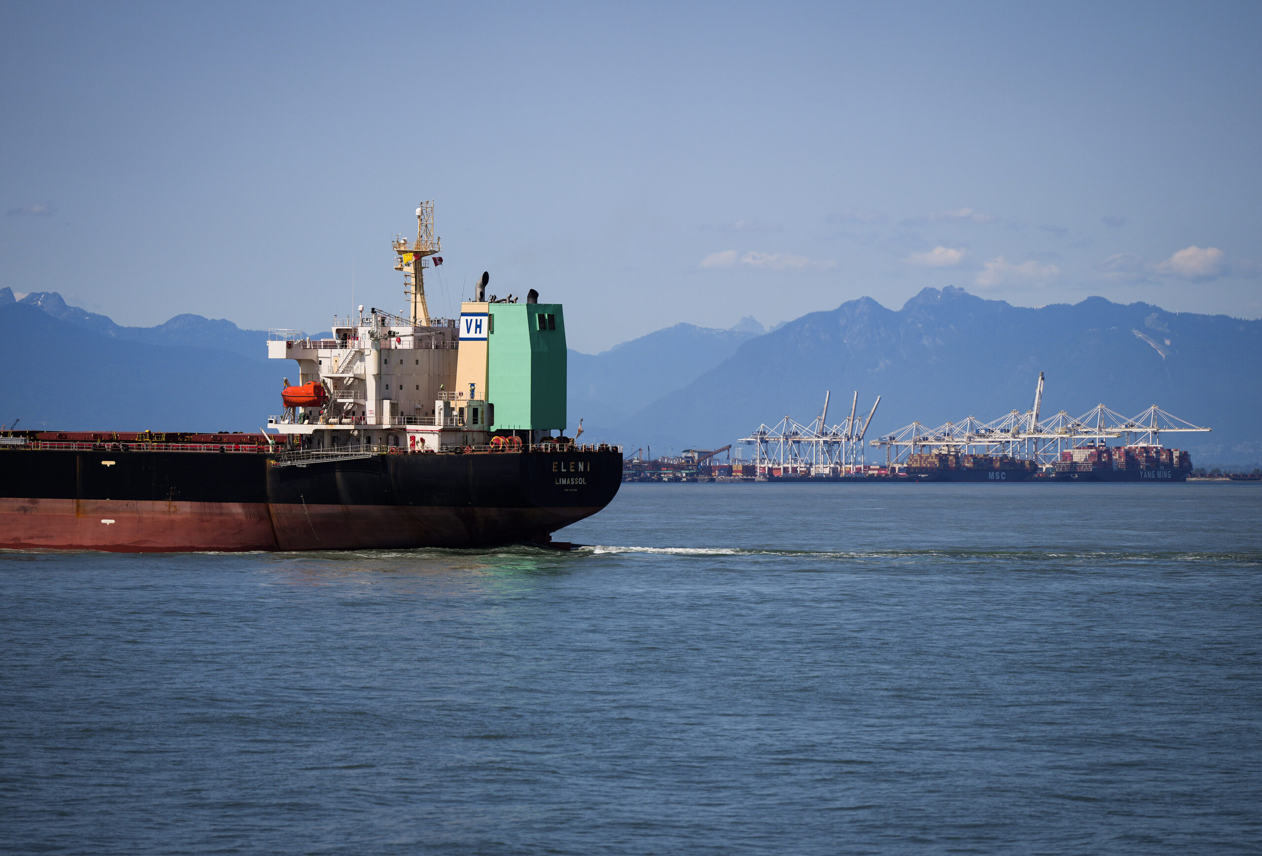 A cargo container ship sails toward Deltaport, Canada's largest container terminal, in Tsawwassen, B.C. on a clear day. The port's gantry cranes and containers can be seen in the background