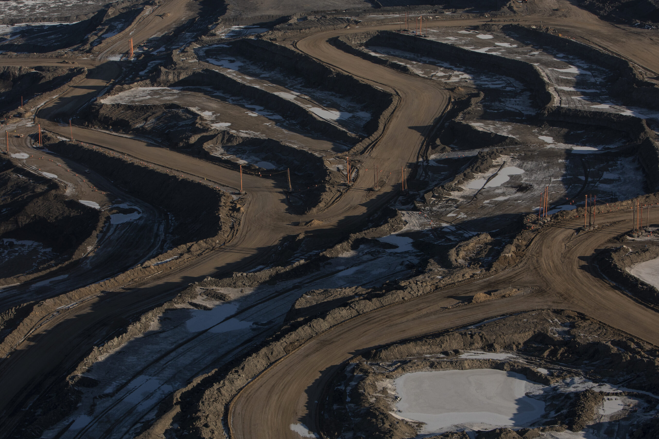 Mud roads carved into the side of a hill with large dump trucks.