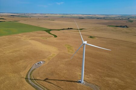 A large wind turbine rises high over flat prairie farmland