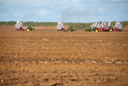 Several tractors equipped with specialized vacuum equipment harvest peat from a cleared field in Manitoba's Washow Bay